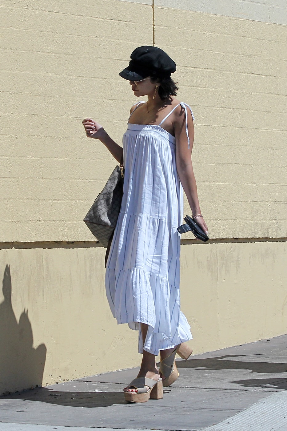 Celebrity fashion: Vanessa Hudgens wearing a white linen dress, oversized tote bag, baker boy cap in black, and chunky platform heels