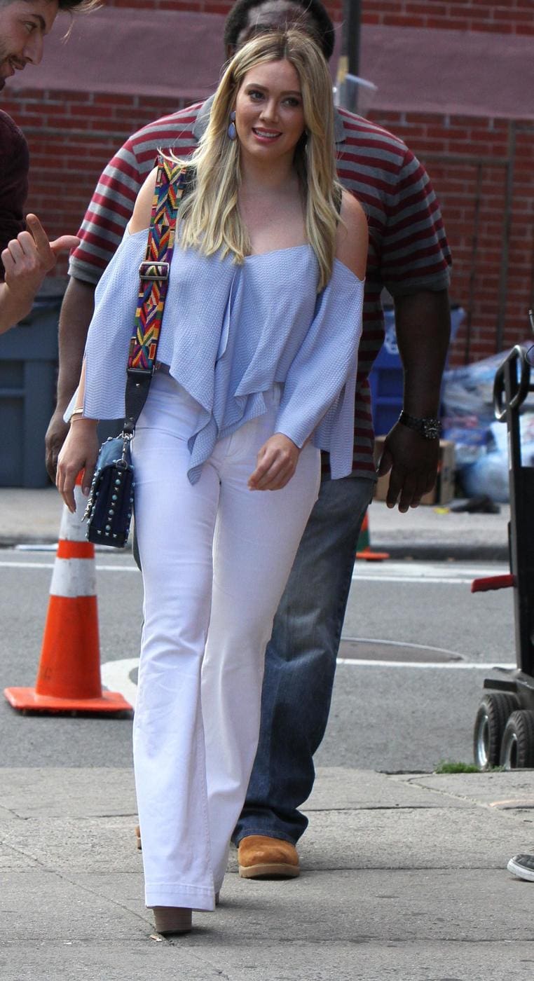 Hilary Duff wearing an off shoulder blue top, white flared jeans, and chunky heels