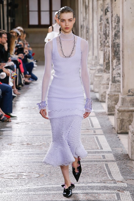 Proenza Schouler Spring 2018 model on the runway wearing a long lilac skirt with ruffles, a sheer lilac tunic, a statement necklace, clear lilac bracelets, and black patent ruffle flats with pointed toes