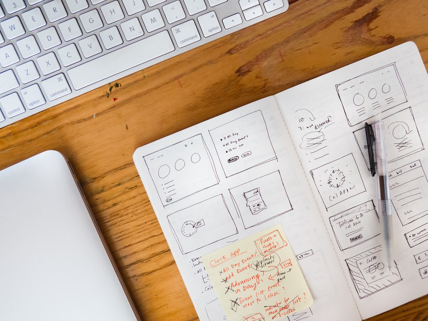 Photo of laptop keyboard, a notebook with writing and a sticky note, and a pen.