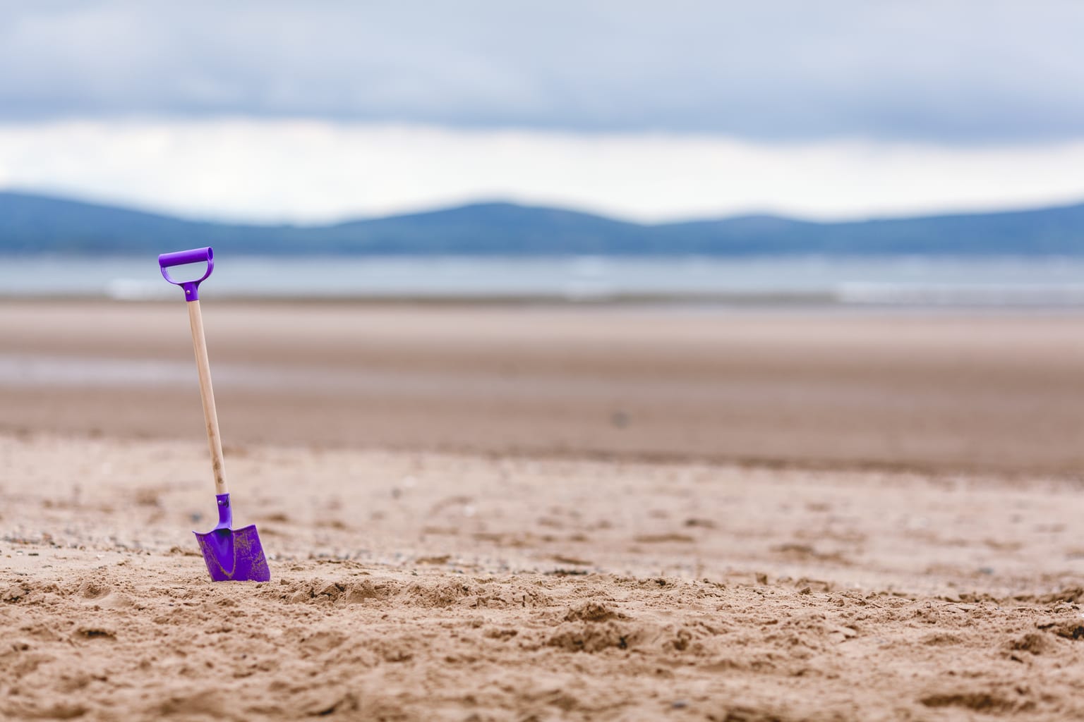 Beach activities: Fun things to do at the beach. Picture of a purple shovel in the sand at a beach.