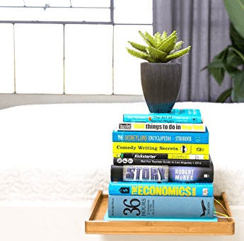 bamboo bed shelf with stacks of books and a plant on top