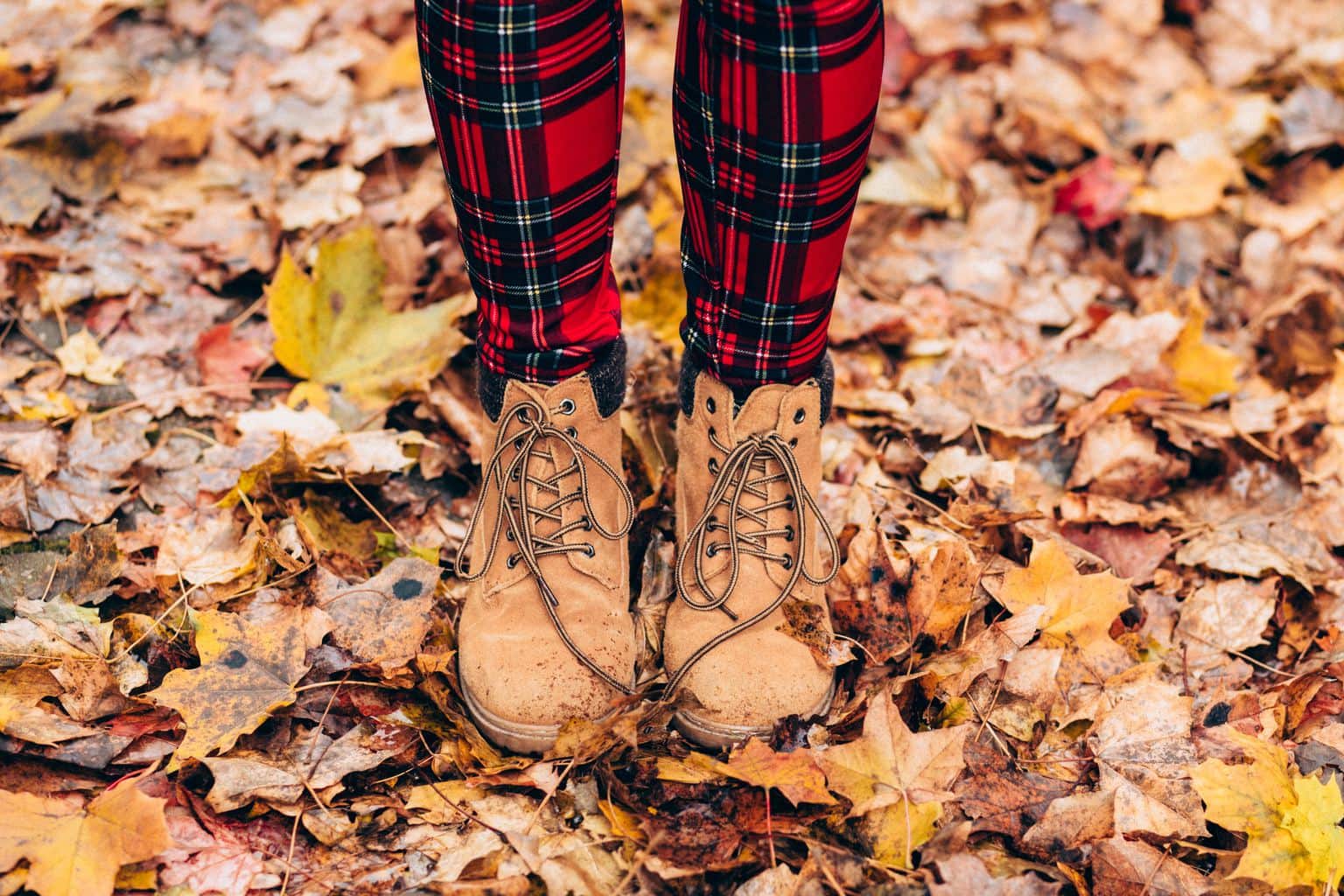 Lady's legs with red plaid leggings and tan boots amongst fallen leaves.