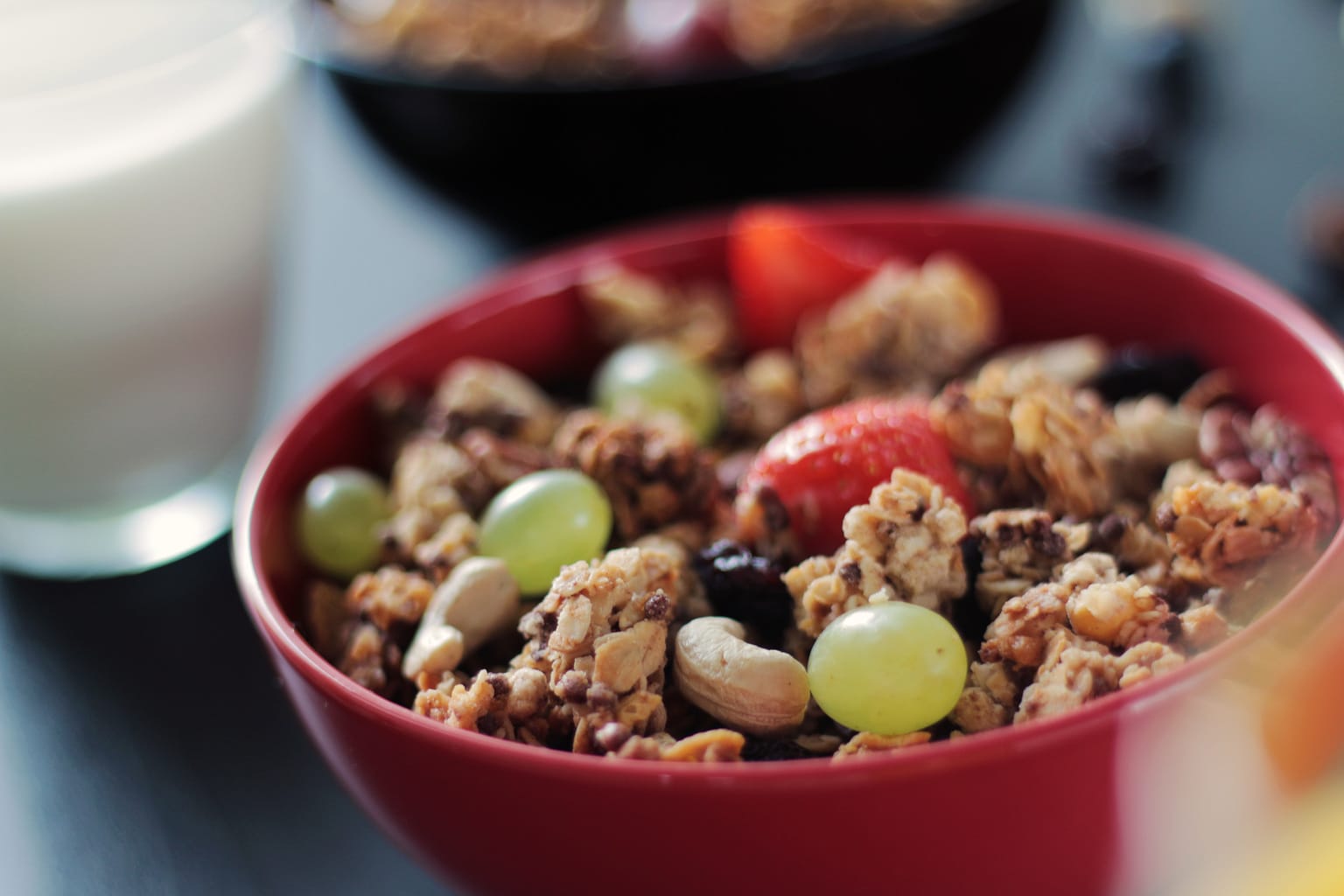 red bowl filled with granola, grapes, cashews, strawberries