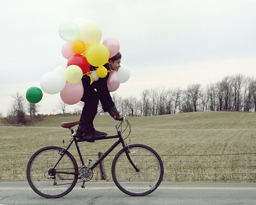 Boy riding a bicycle and carrying balloons