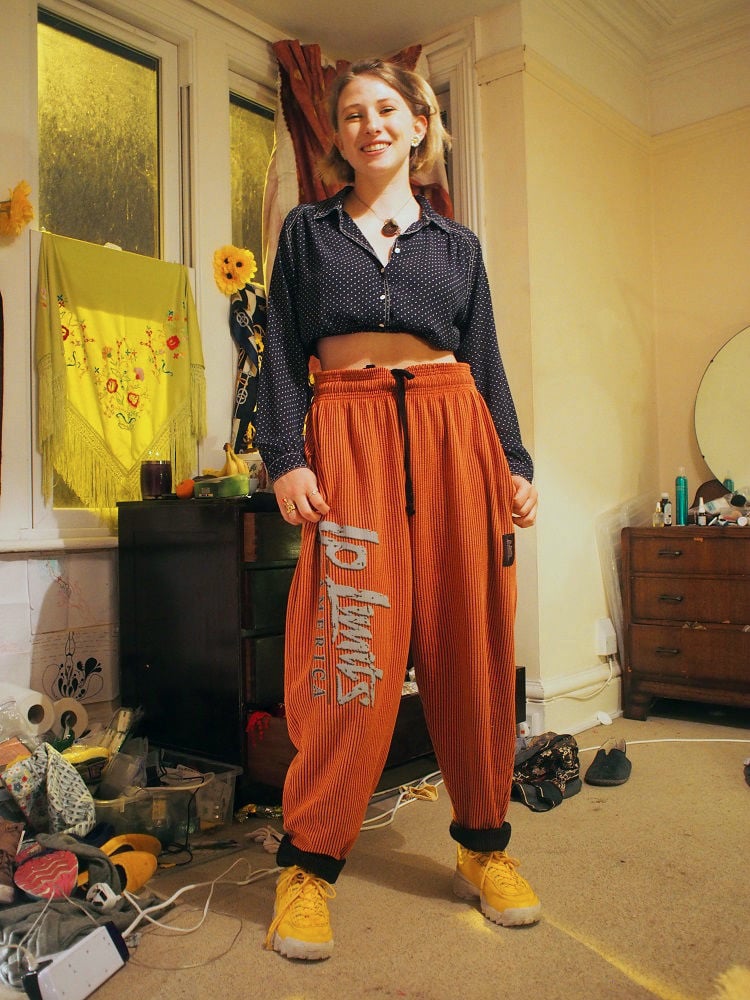 Martha sports a cropped navy polka dot button-up blouse with thick high-waisted oversized orange jogger pants, and chunky yellow sneakers.