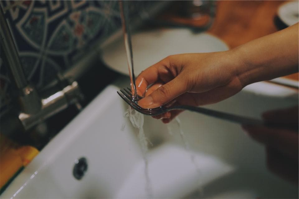 Photo of person washing a fork. Colorful tile in background as well as a dirty plate.