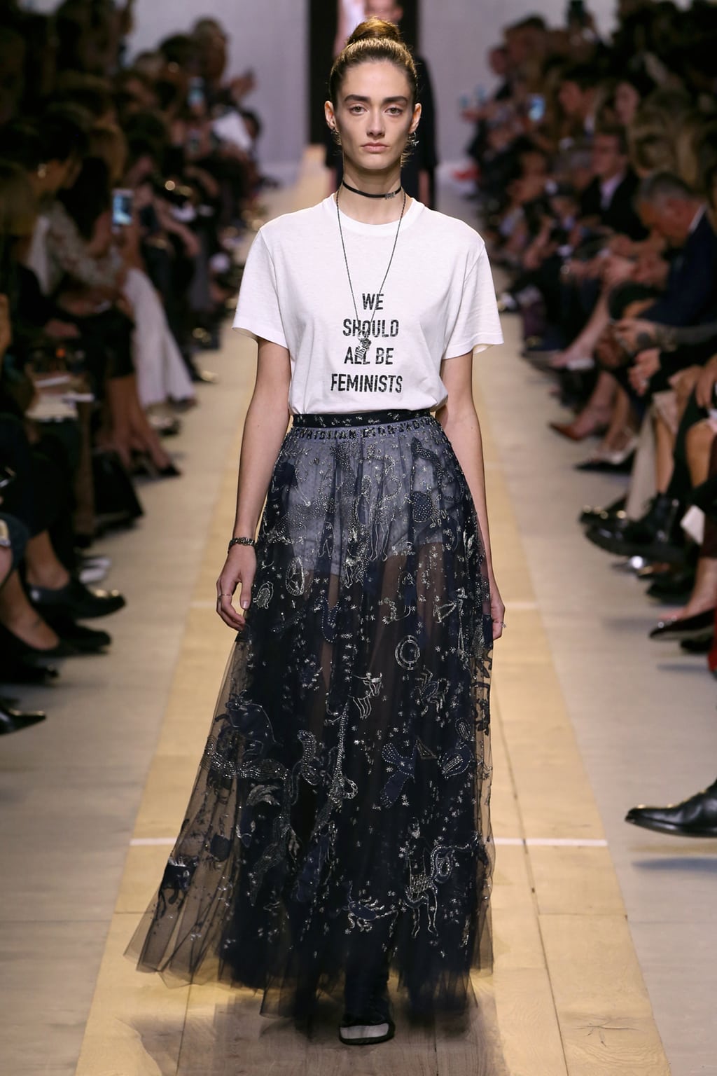 Dior Spring 2017 look 2: Model wearing a We Should All Be Feminists tee shirt, navy embroidered tulle skirt, and chokers