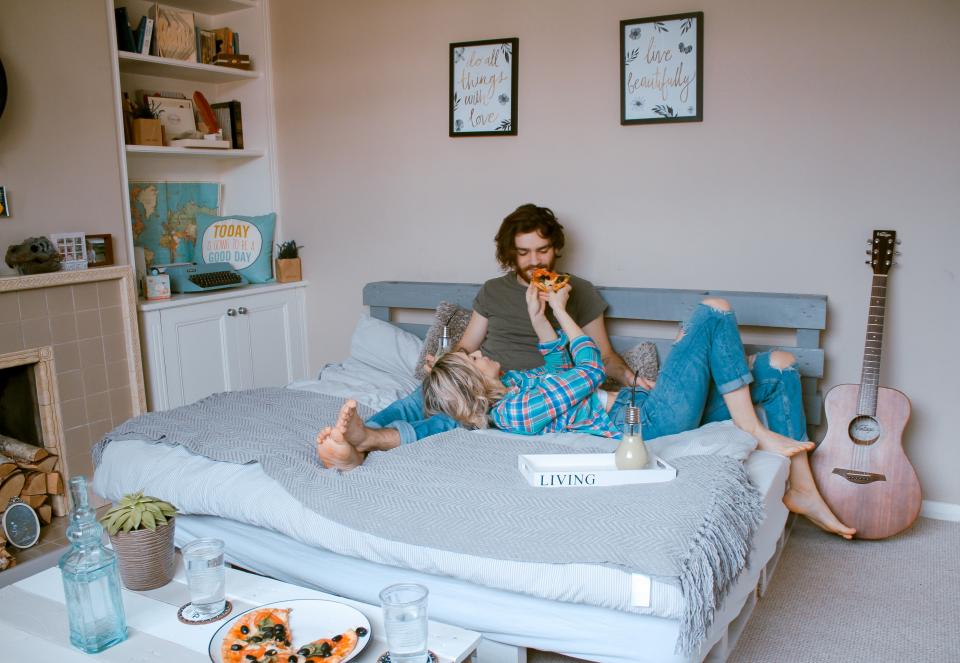 Woman feeding man pizza in bed