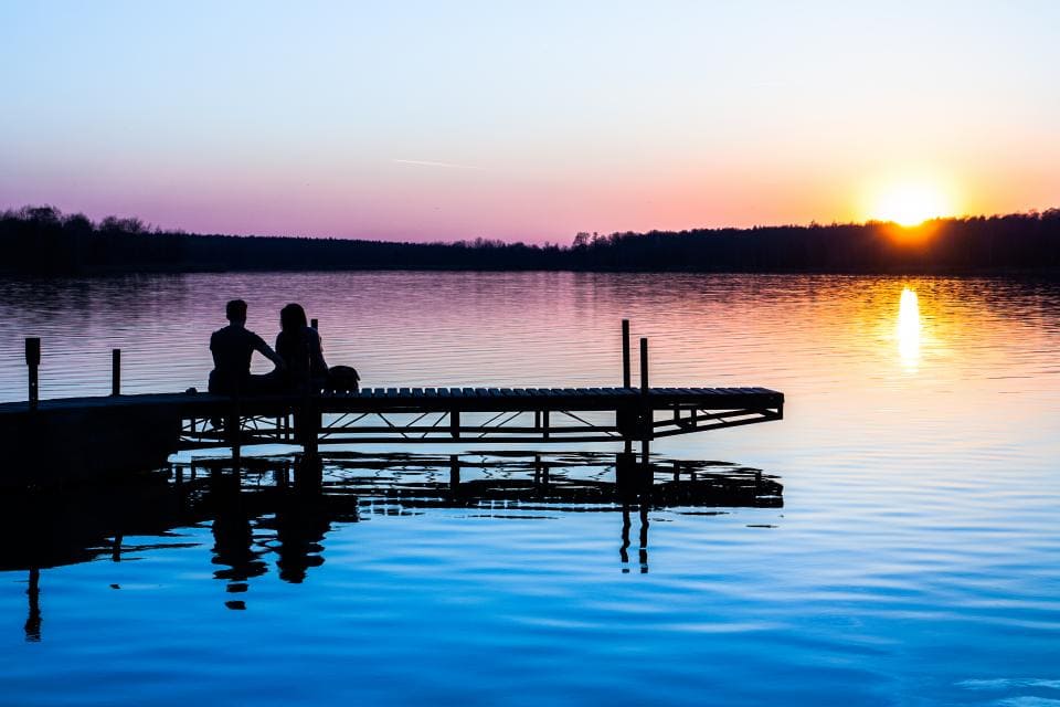 Couple on lake, sitting on pier, watching the sunset