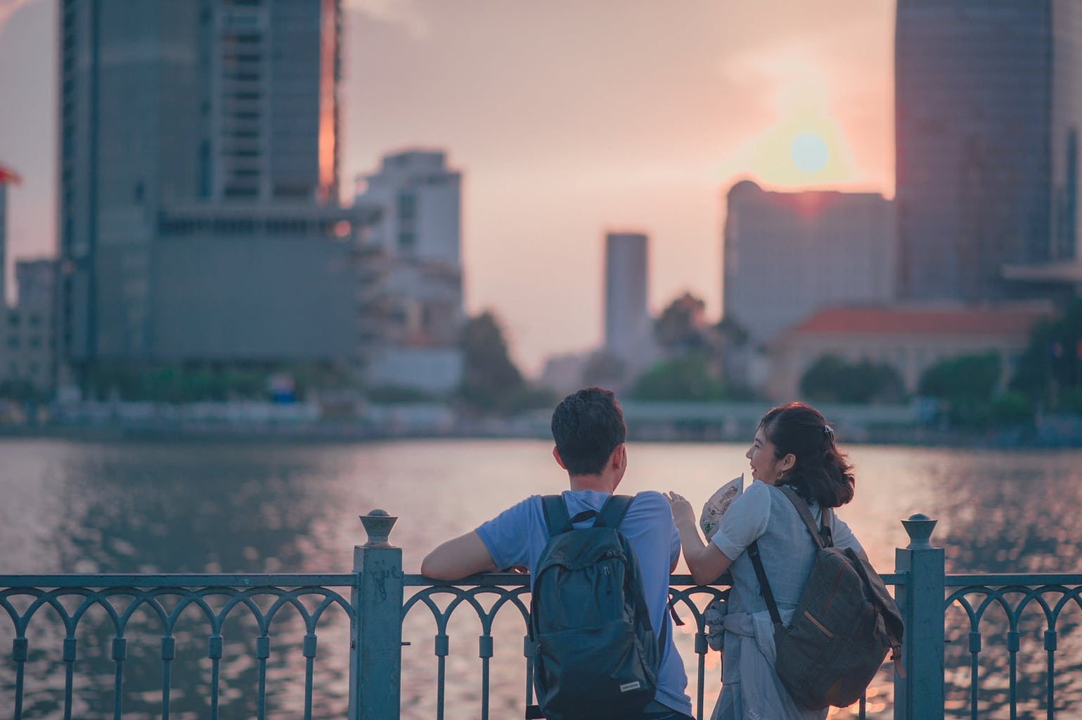 Boy and girl wearing backpacks having a conversation overlooking a river at sunset