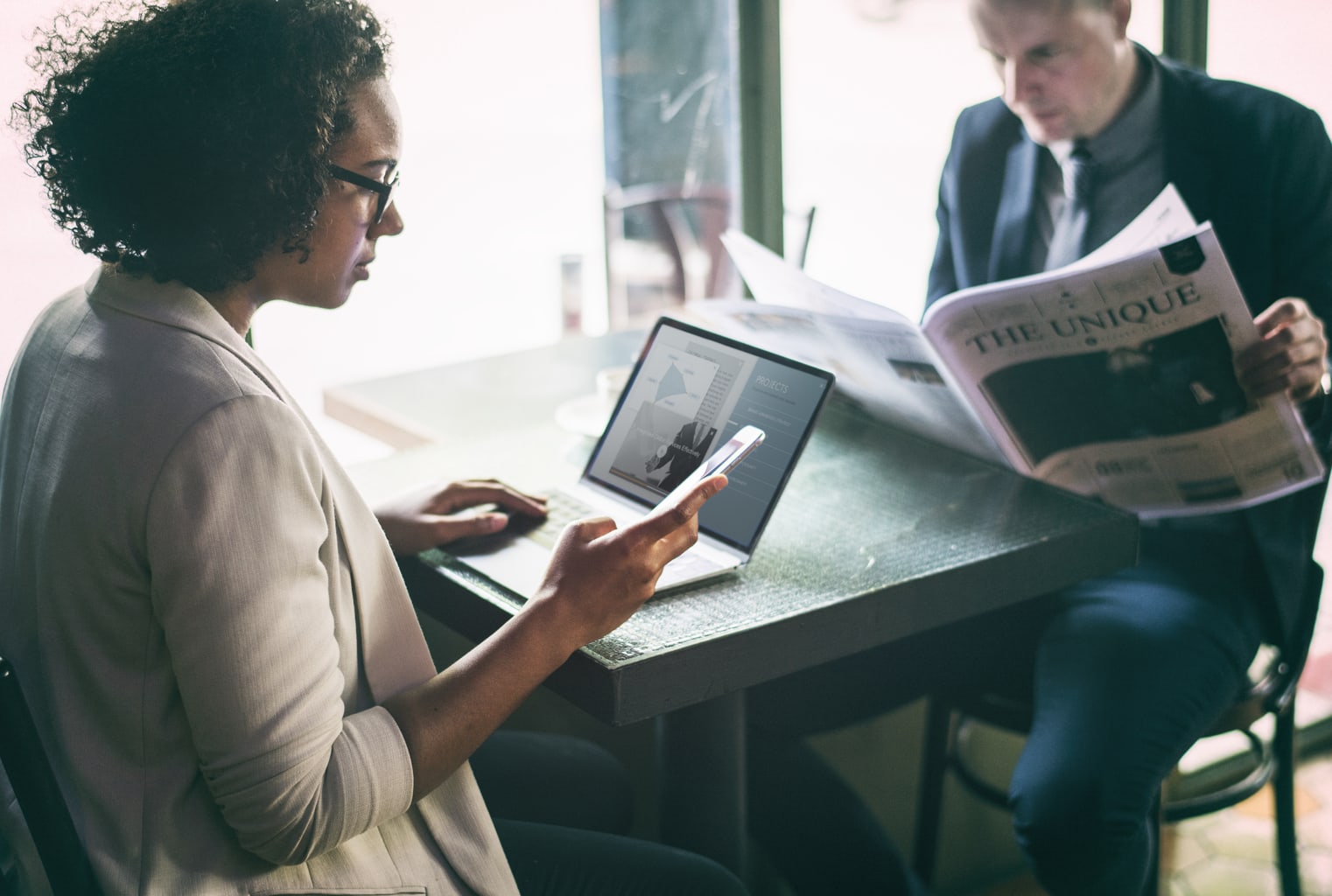 Photo of girl with curly hair at a coffee shop using her phone and computer.