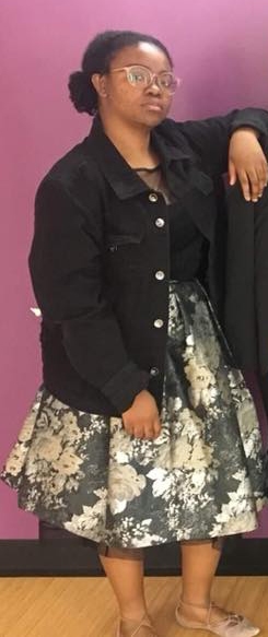 College student wearing glasses, an oversized denim jacket, and a wide skirt