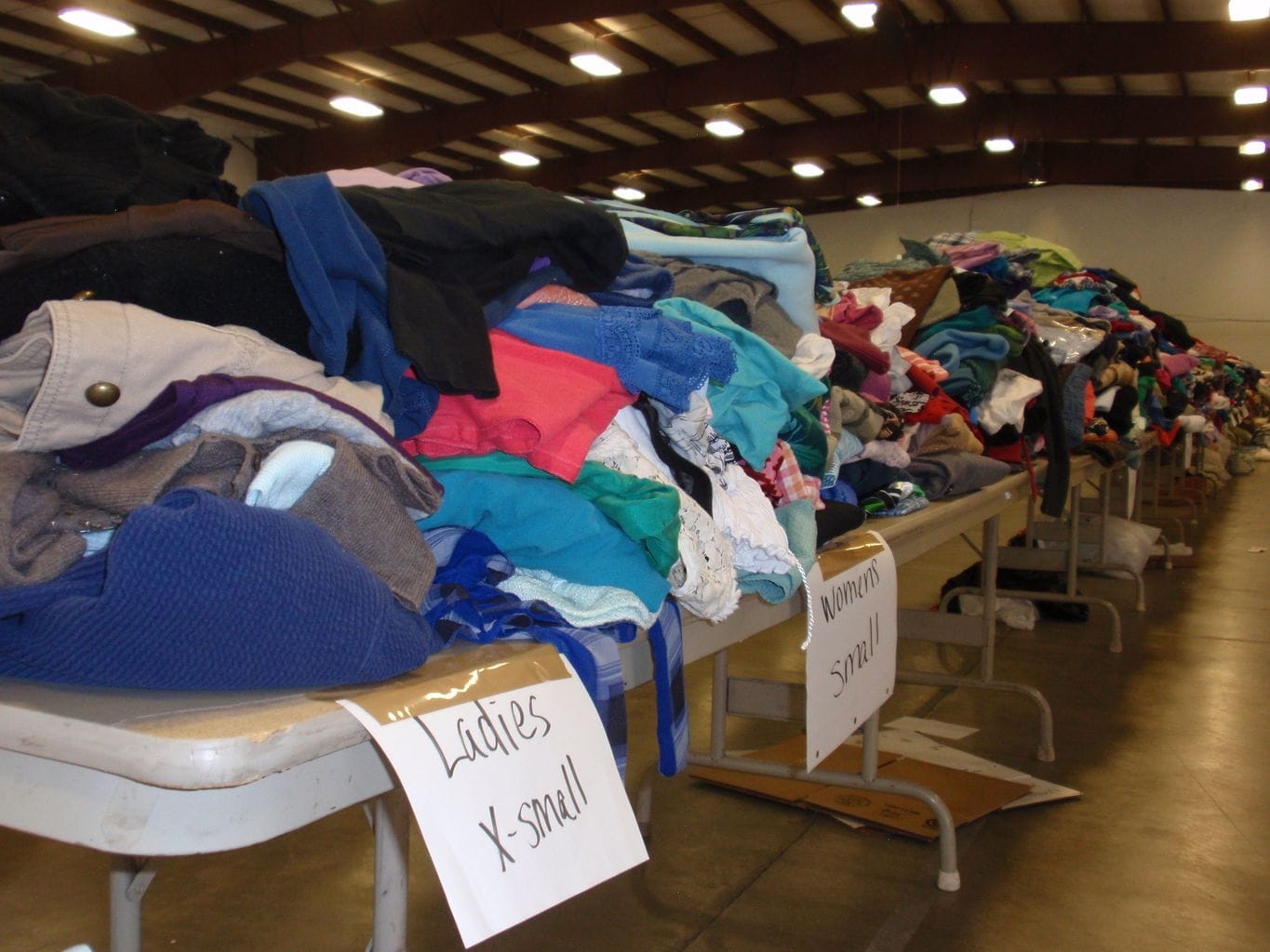 Photo including various clothing items stacked/piled on a table.