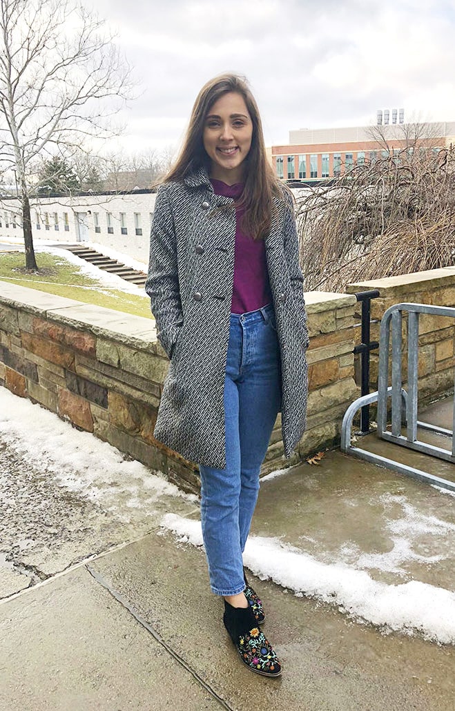 West Virginia University student wears a fashionable cold-weather outfit of an eggplant thrifted sweater, high-waisted mom jeans, and black embroidered floral booties with a black and white trench coat.