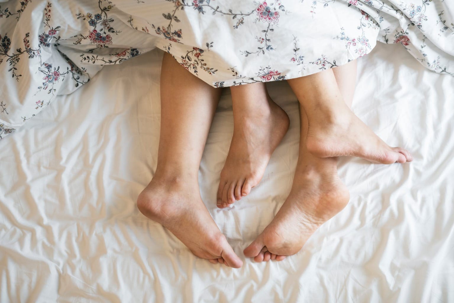 Two peoples' feet in a bed with a floral comforter