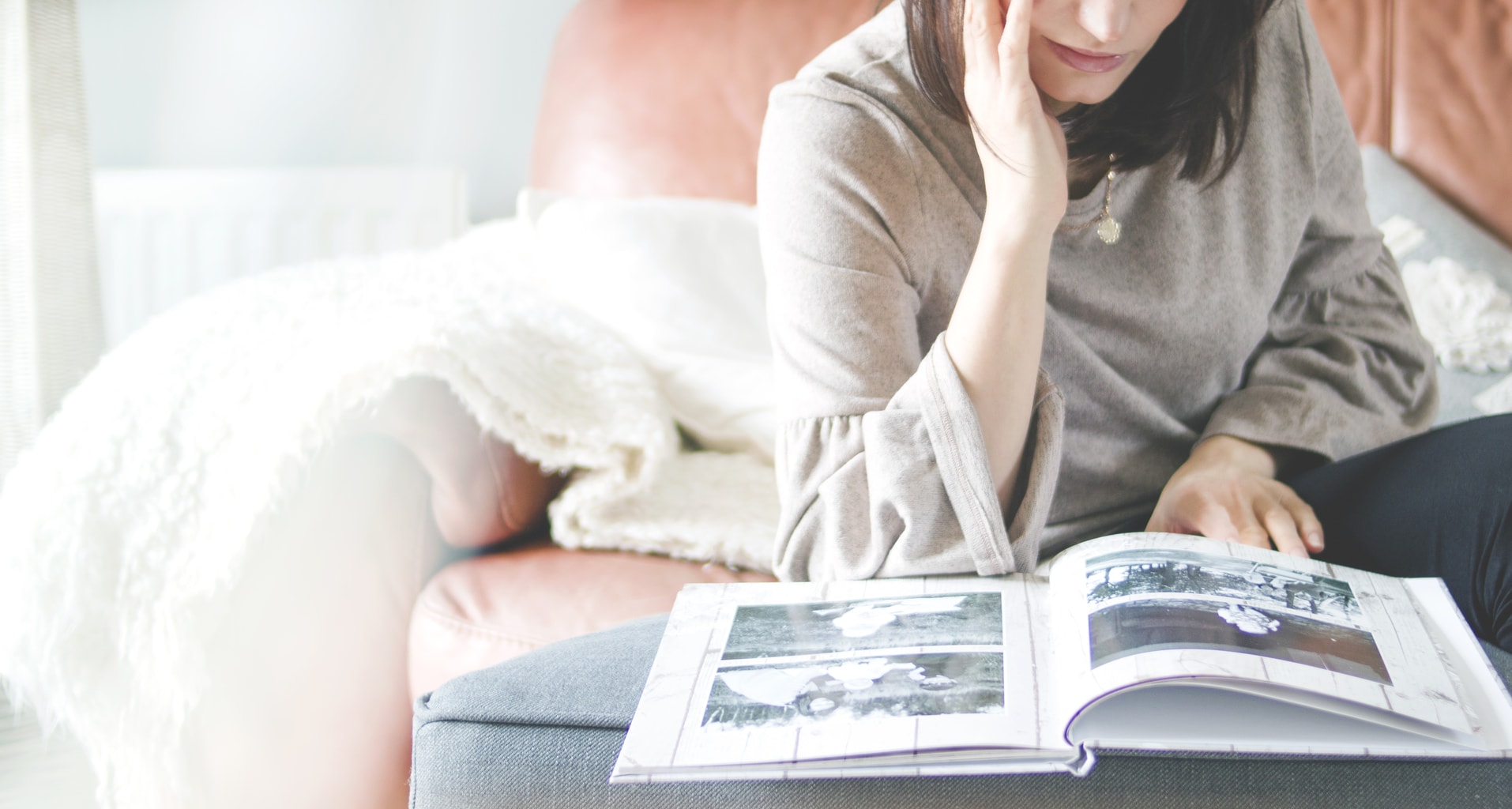 Girl with brown hair reading a book in a red chair with a white throw.