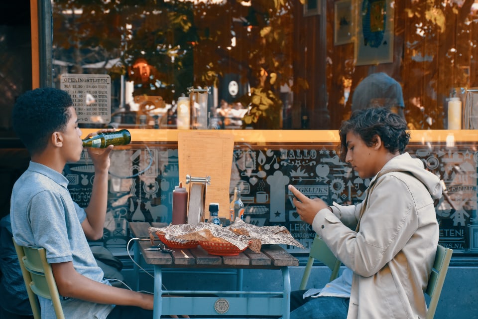 Friends eating lunch, one drinking, other on phone