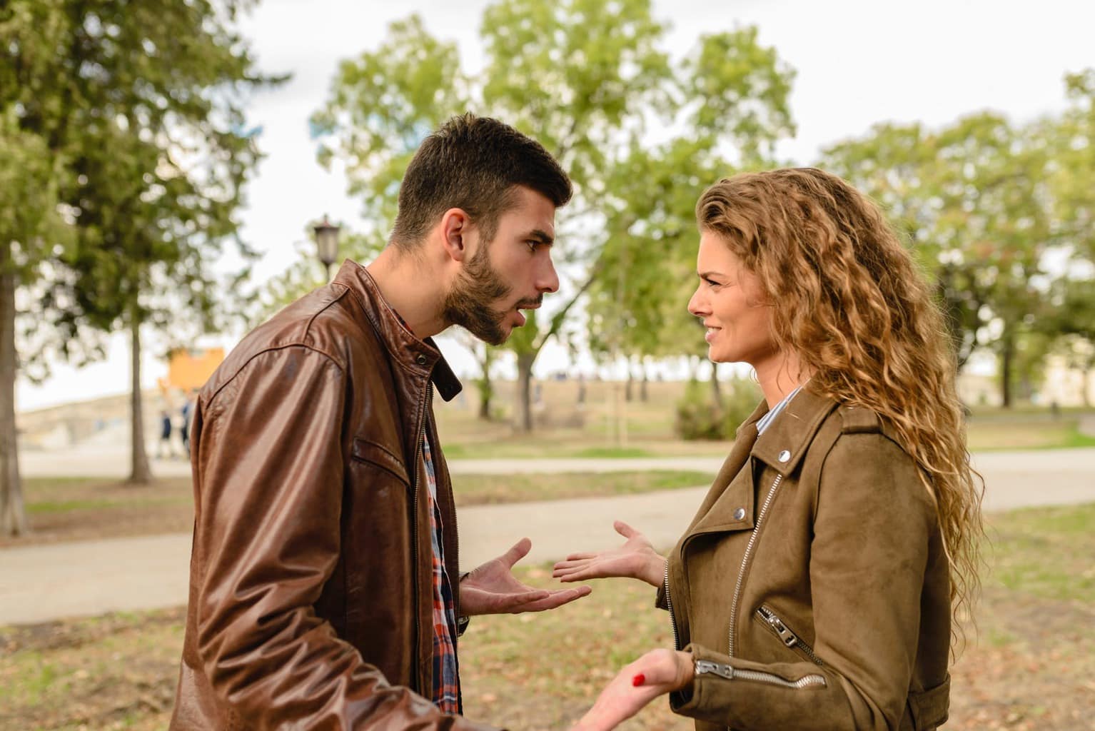 Man and a woman fighting in a park, wearing brown coats