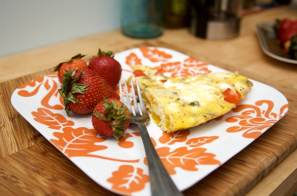 A slice of frittata on a plate with strawberries and a fork