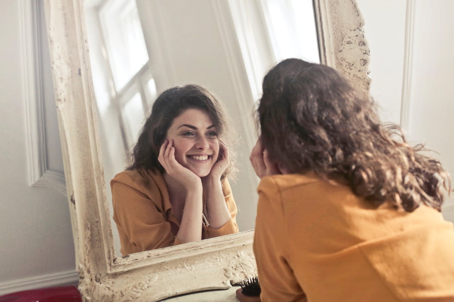 Girl in a yellow shirt staring at herself and smiling in a mirror