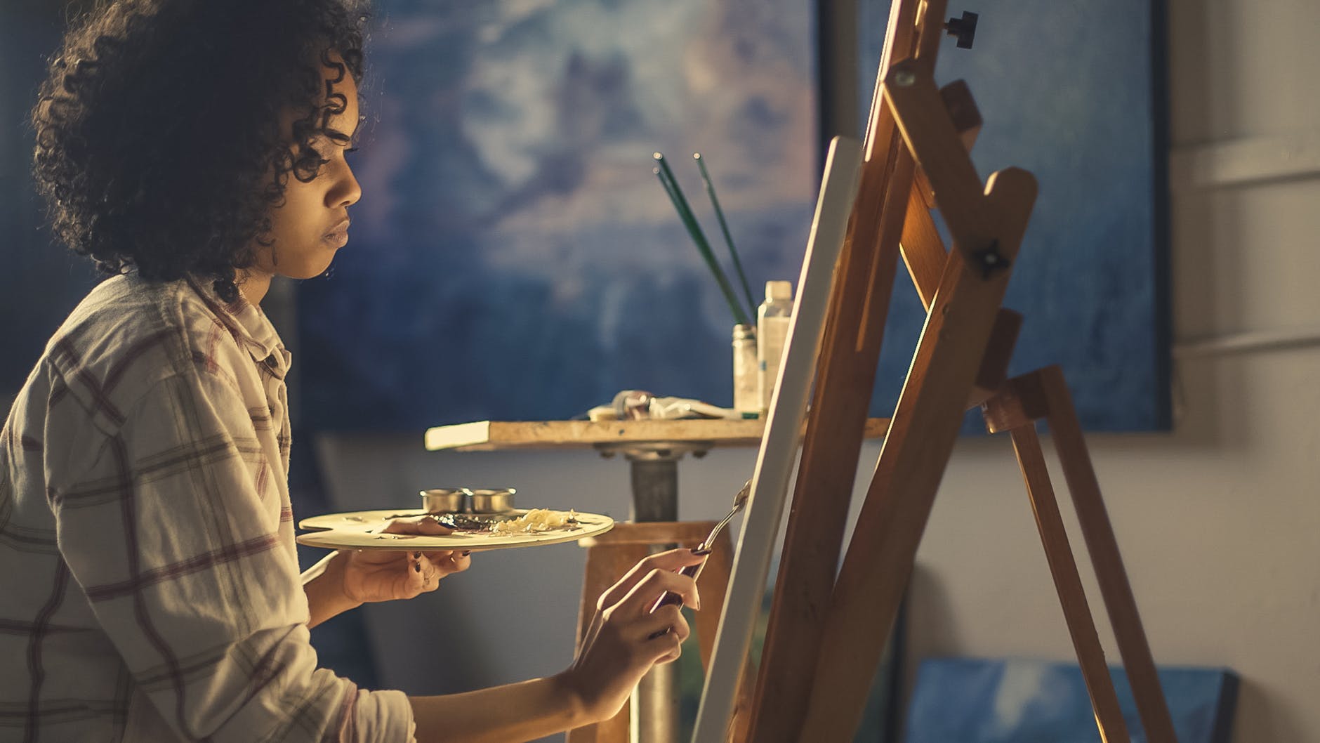 Girl in white shirt painting on an easel with blue painting in background