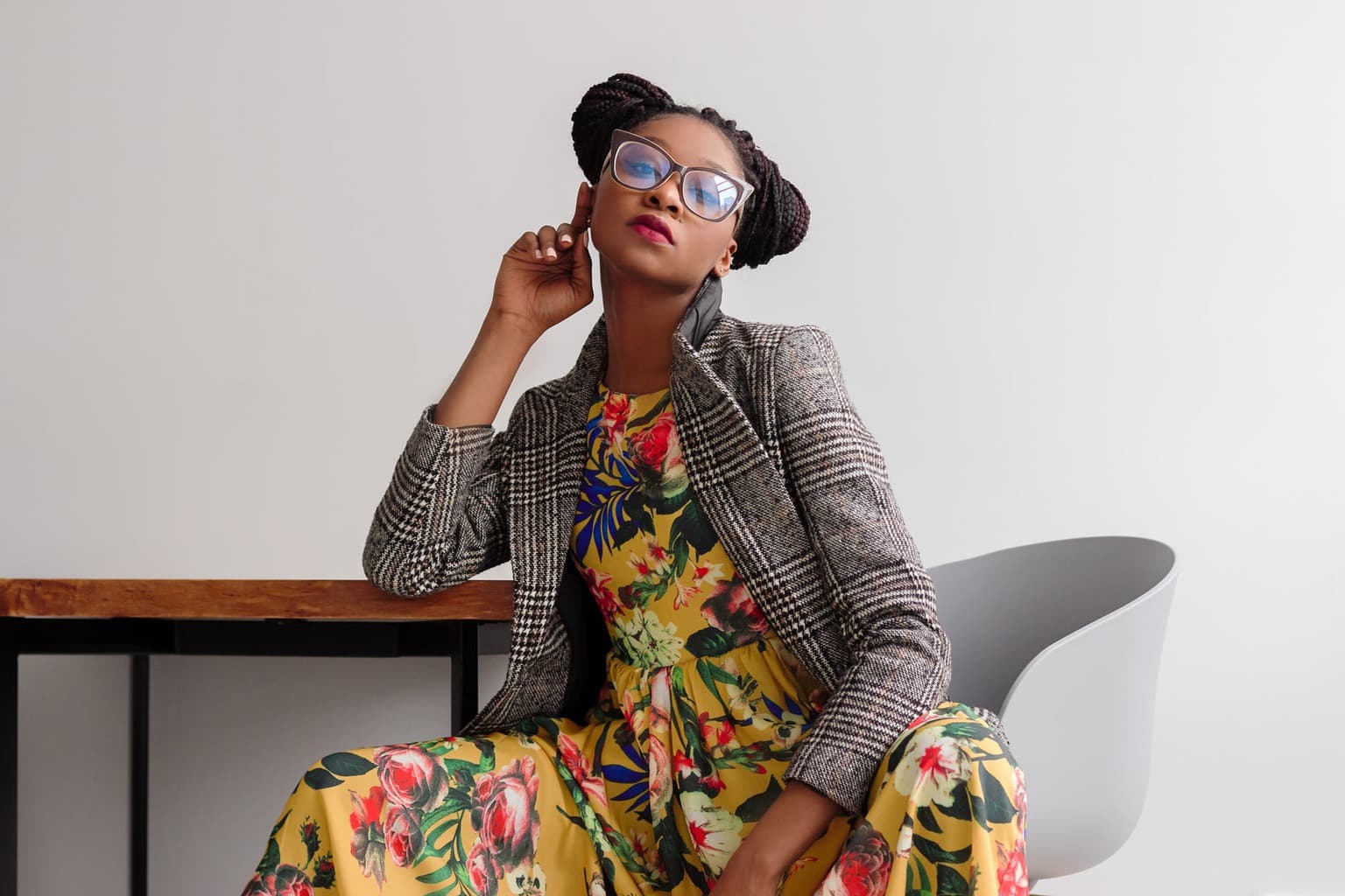 Woman sitting on a chair with a plaid blazer and a yellow dress and glasses