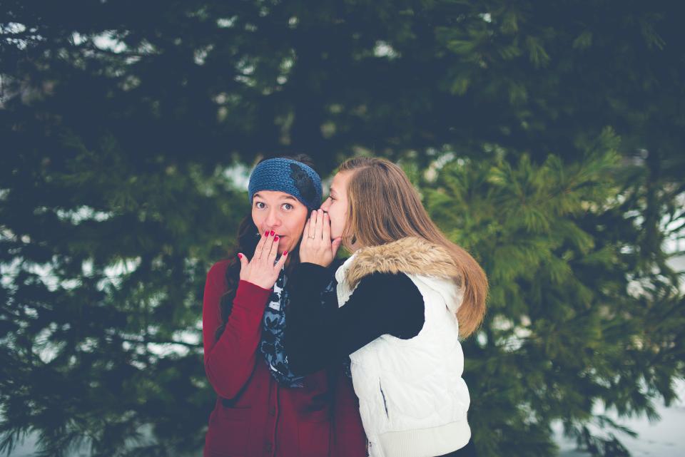 Girls whispering in the snow in front of a tree