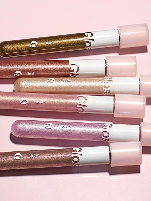 Close-up photo of Glossier Lidstar in shades (from top to bottom) Herb, "a smoky green with yellow gold pearl"; Cub, "a smoky green with yellow gold pearl"; Moon, "the sheerest cream base with blueish opalescent glimmer"; Slip, "a sheer baby pink with golden highlight effect"; Lily, "a sheer lilac base with blue and violet pearls"; and Fawn, a cool, smoky taupe with violet and neutral gold pearls