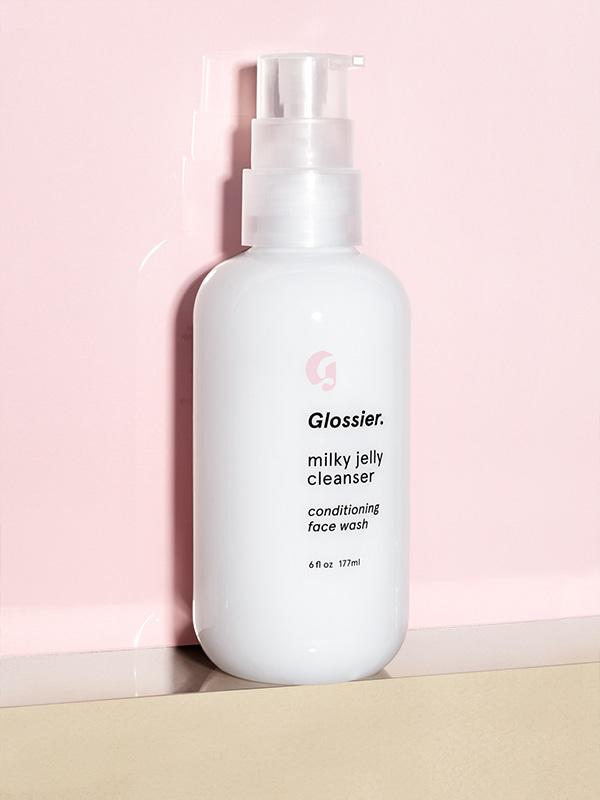 Photo of Glossier Milky Jelly Cleanser resting on beige surface against Millennial Pink background