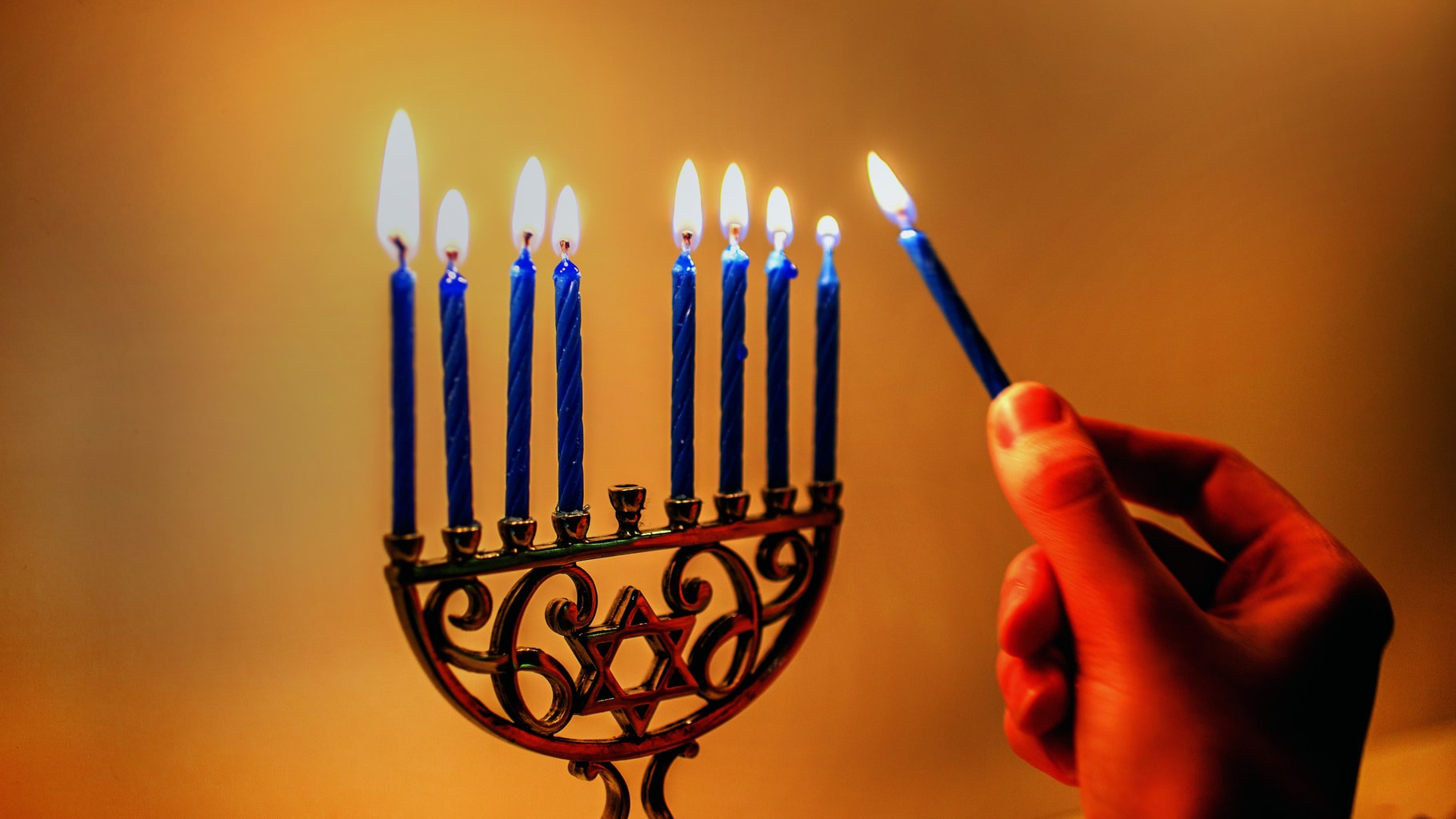 Woman lighting a small Hanukkah menorah with blue candles