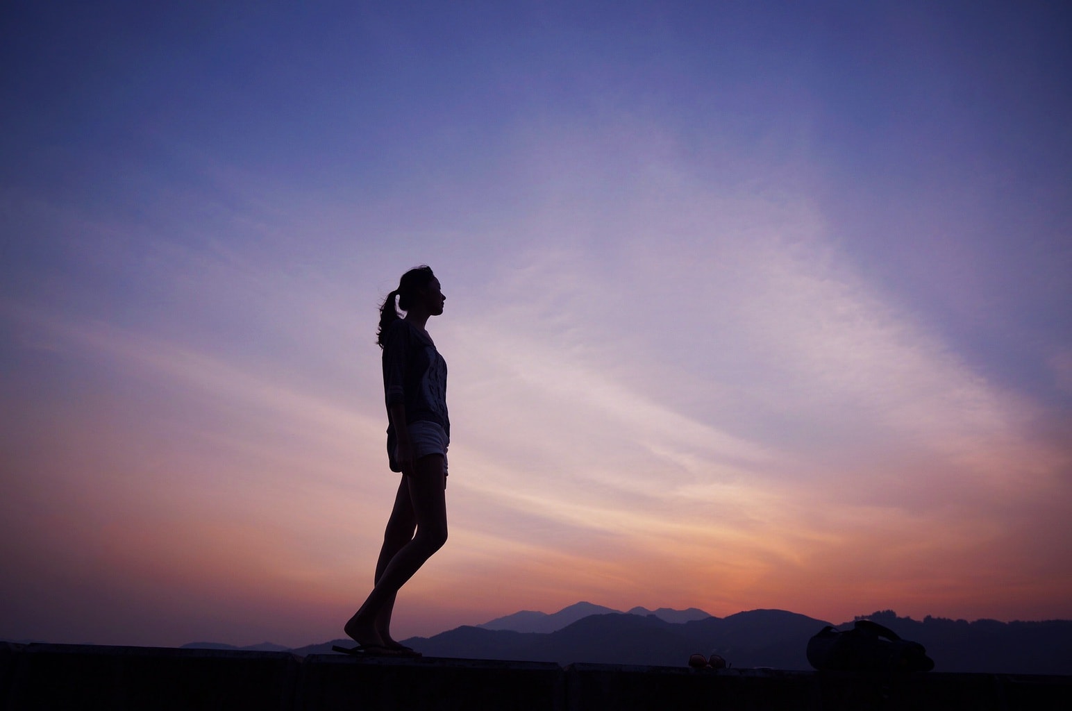 Introverted girl standing alone on a mountain in front of a sunset