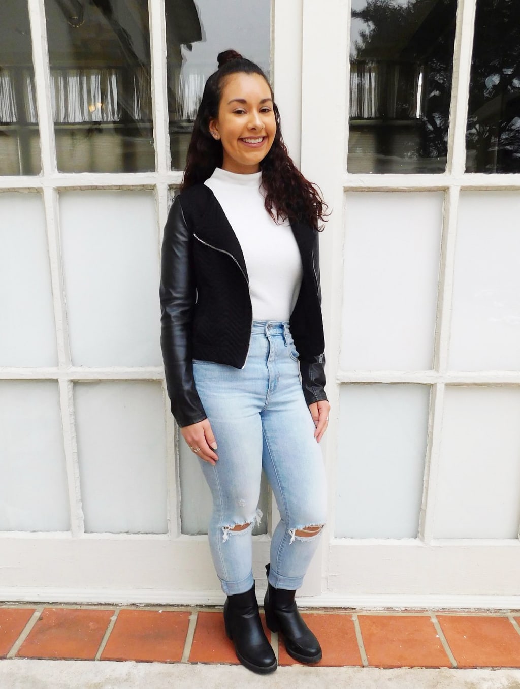 Jefferson University student Jackie styles her simple white turtleneck sweater with a black motorcycle jacket with silver zipper detailing, a pair of high-waisted light-wash denim jeans with distressed knees, and a pair of chunky-heeled booties.