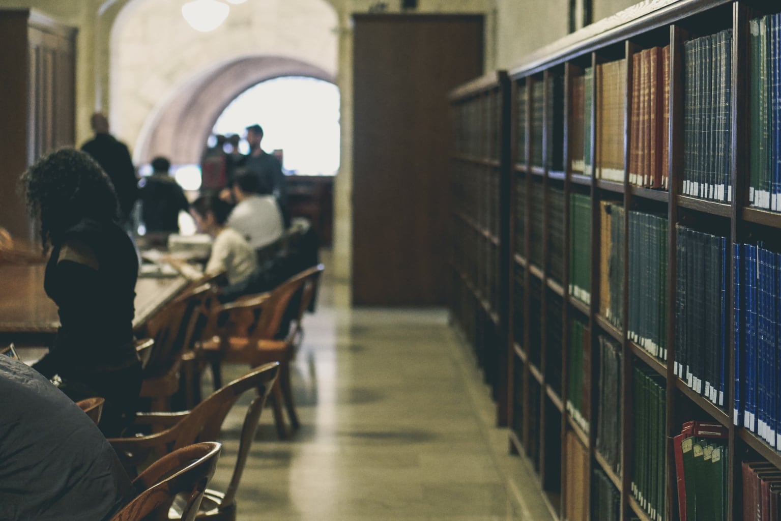 People work at library tables with a view of book shelves to the side