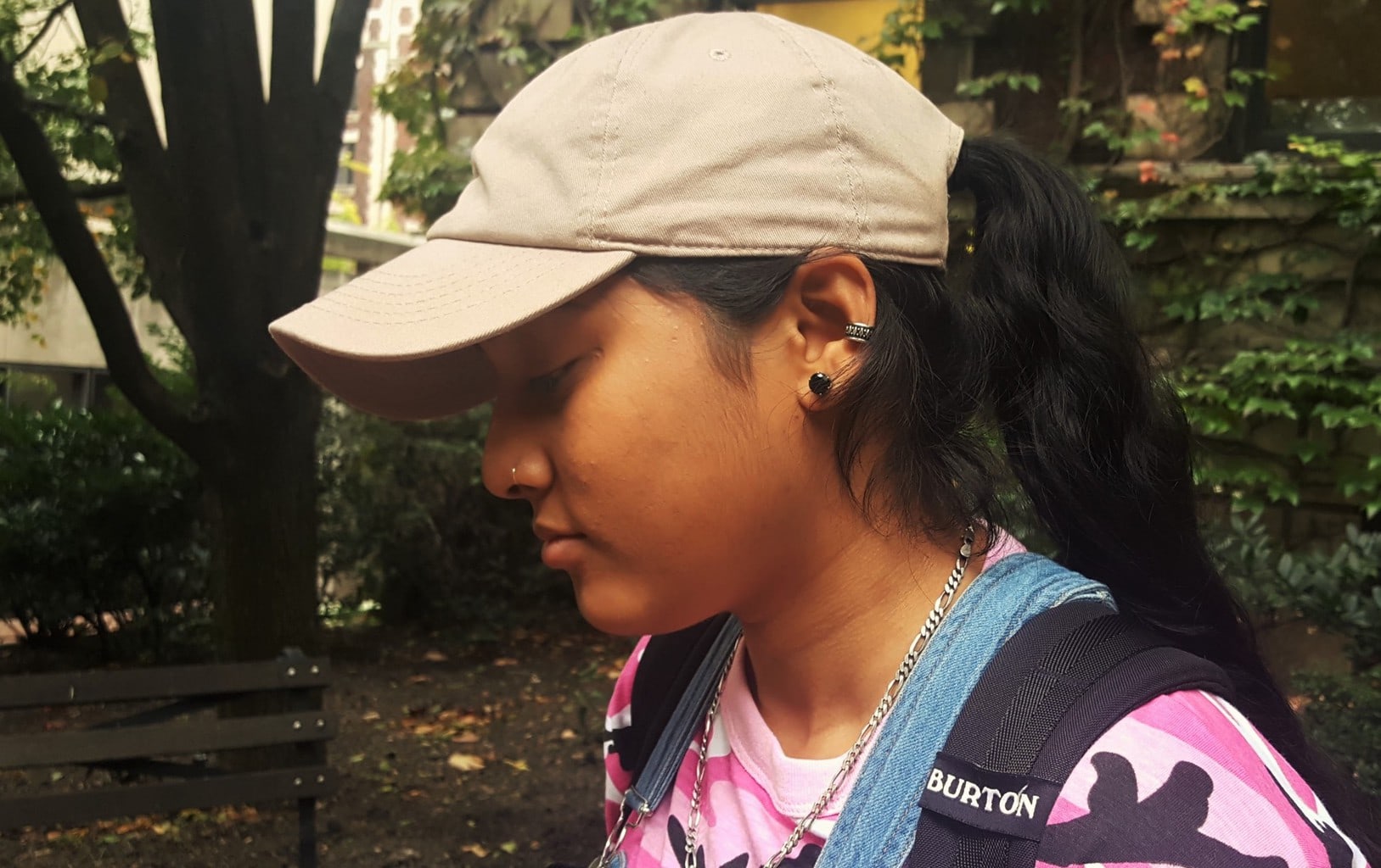 Alema wears a tan baseball cap with her black stud earrings and cartilage piercing.