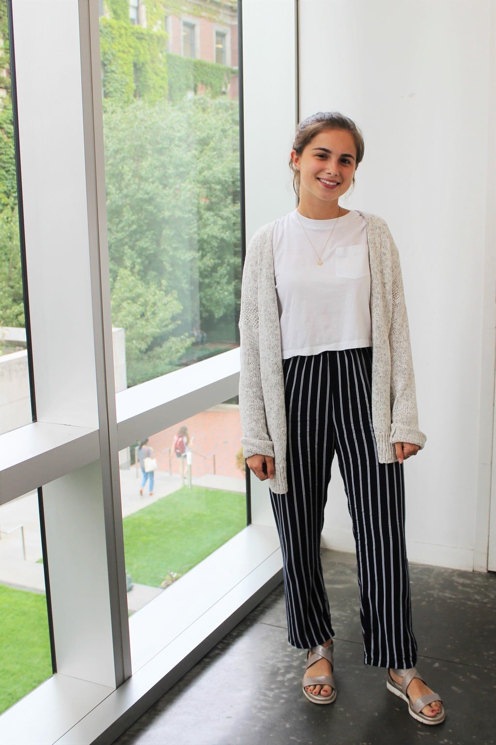 Maya, a student at Barnard College at Columbia University, sports a neutral white crop top, cozy off-white oversized cardigan, vertically striped black and white pants, and silver sandals.