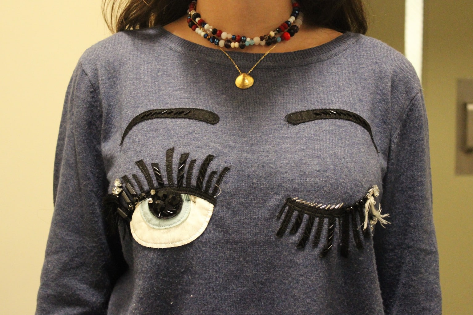 Rachel wears a one-of-a-kind grey winking eye sweater.