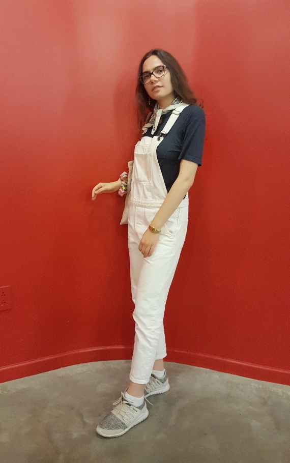 Columbia University Student Style: white overalls with a navy t-shirt underneath, accented by a white bandana necktie and grey sneakers for comfort.