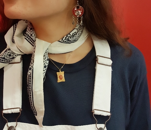 A white necktie contrasts with a navy t-shirt, paired with a simple gold necklace with square pendant and red chandelier earrings.