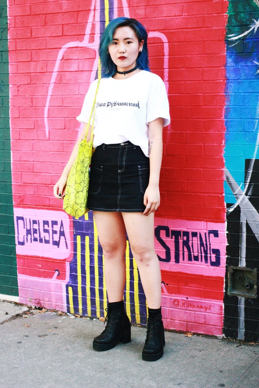 Fashion Institute of Technology with teal blue hair wears a grunge look that consists of a baggy white t-shirt and a black skirt, complete with choker and chunky combat boots.