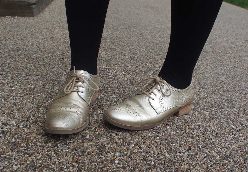 Hannah's shoes are gold lace-up oxfords which she wears with black tights.