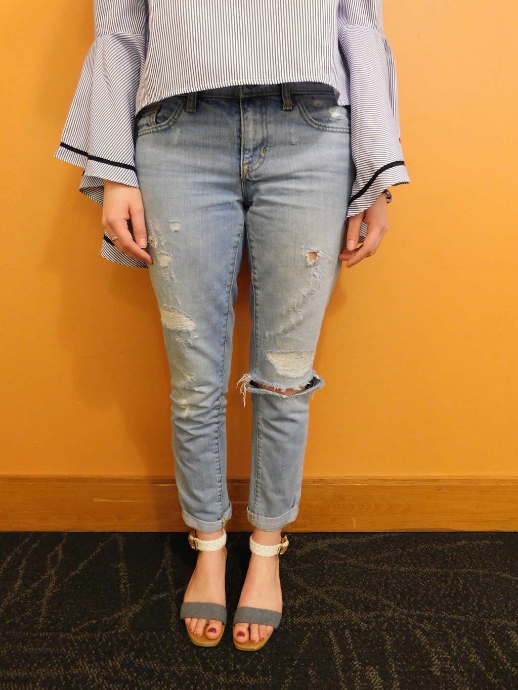 Danielle wears light-wash distressed denim jeans cuffed up with white and grey flat sandals.