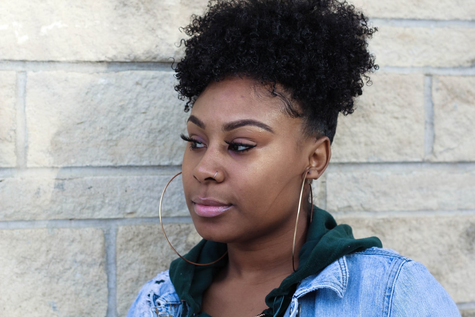 Chaunice wears ultra-large thin gold hoop earrings and a fresh face of makeup with light pink eyeshadow and lipstick, long eyelashes, defined eyebrows, and shimmering dewey highlighter.