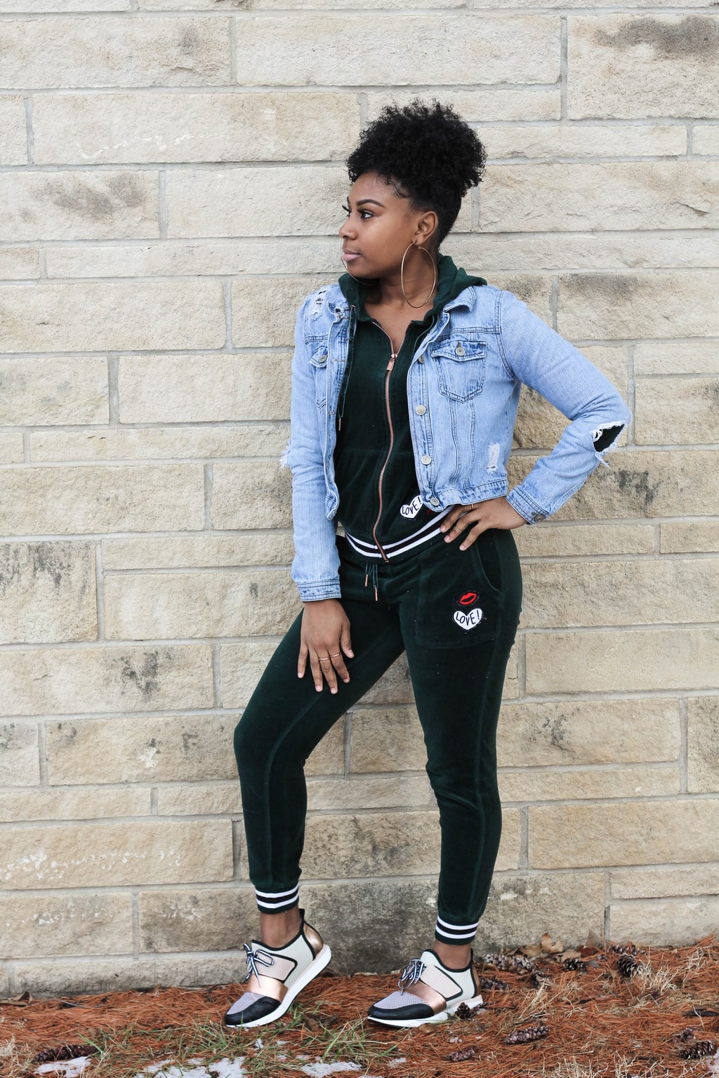 Kansas State University student Chaunice wears a green velour athletic sweatsuit with cropped jogger pants with embroidered lips and love patches and a matching hoodie with a rosegold zipper. She layered on a light-wash distressed denim jacket, giant gold hoop earrings, and crisp black, white, and rosegold sneakers.