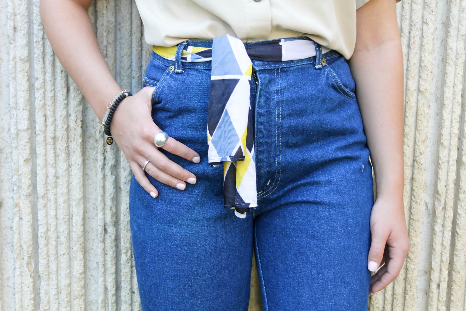 This patterned yellow, light blue, white, and dark blue scarf is tied as a belt around Emilee's high-waisted jeans.