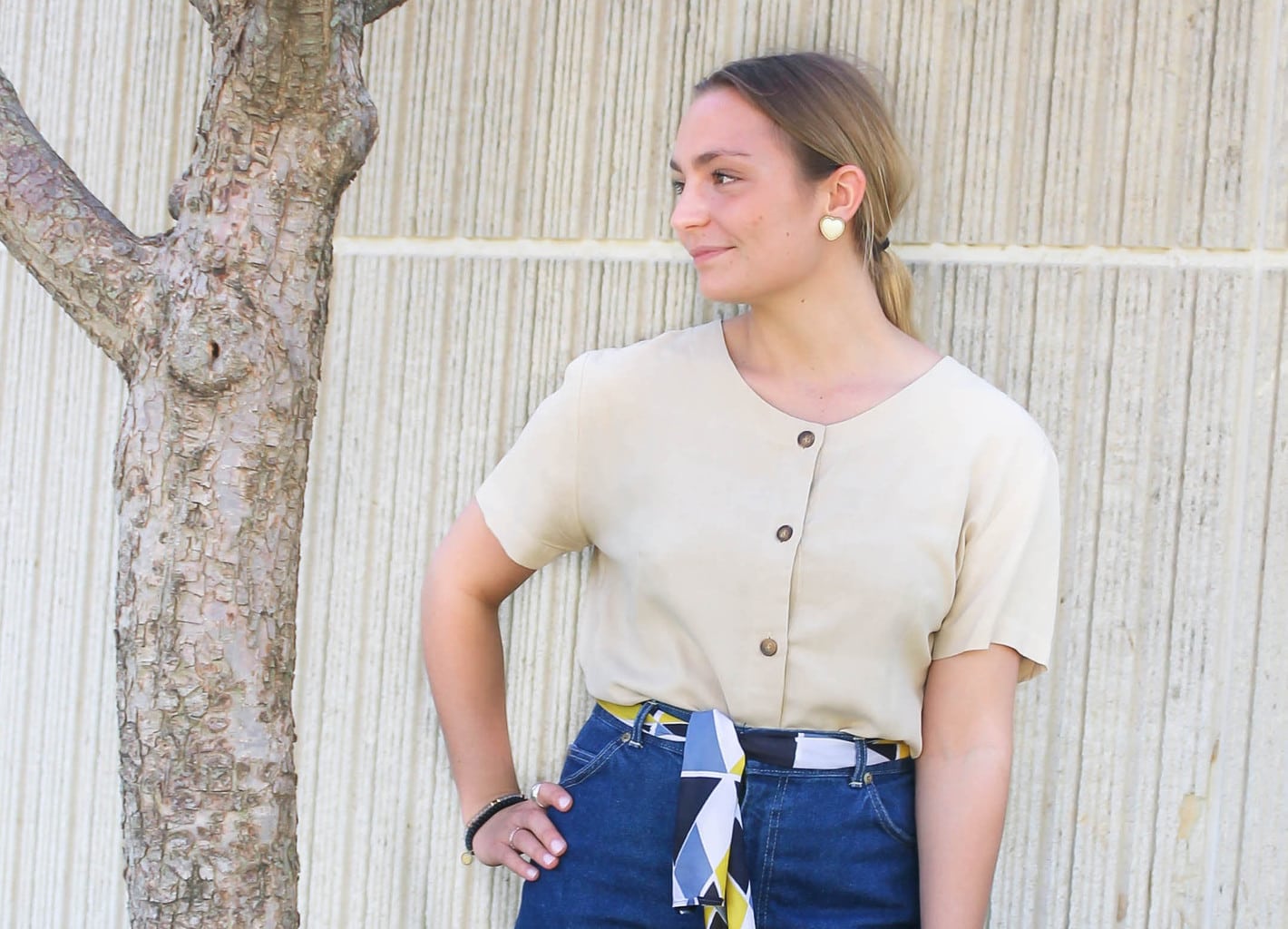 Emilee's pale yellow scoop neck top with brown buttons is tucked into her high-waisted jeans.