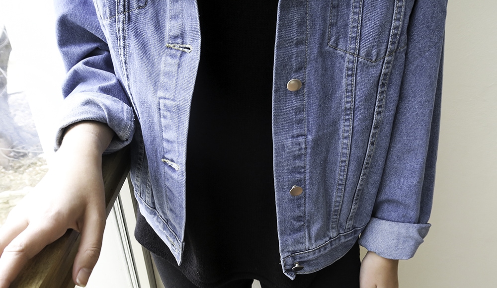 Hannah wears a black tee with a light-wash distressed denim oversized jacket with the sleeves rolled up.