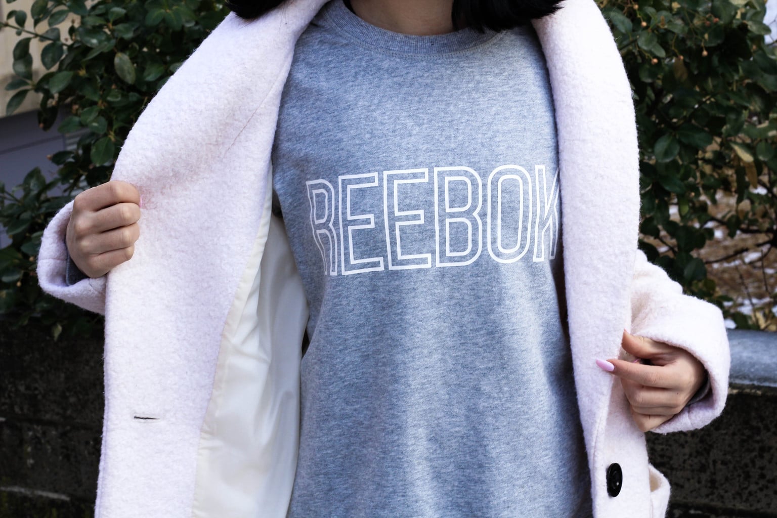 Jessie wears a loose-fitted  casual vintage style grey Reebok tee with her baby pink winter coat.