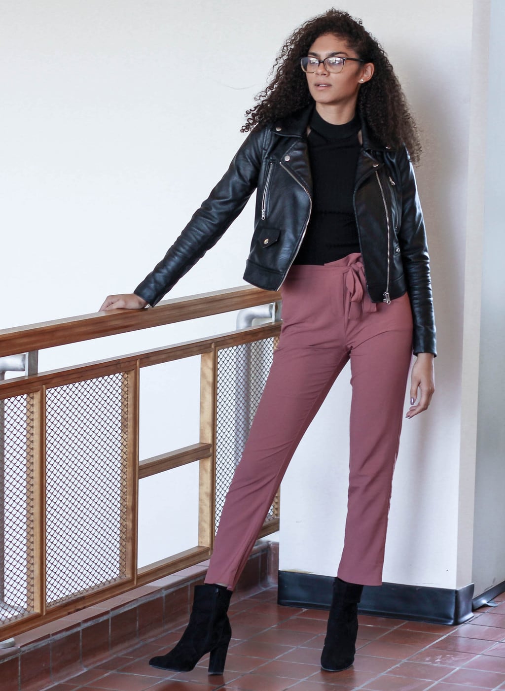 Kansas State University student Kylie rocks a black high-neck halter shirt with faded pink high-waisted trousers, a black motorcycle jacket, and tall black booties.