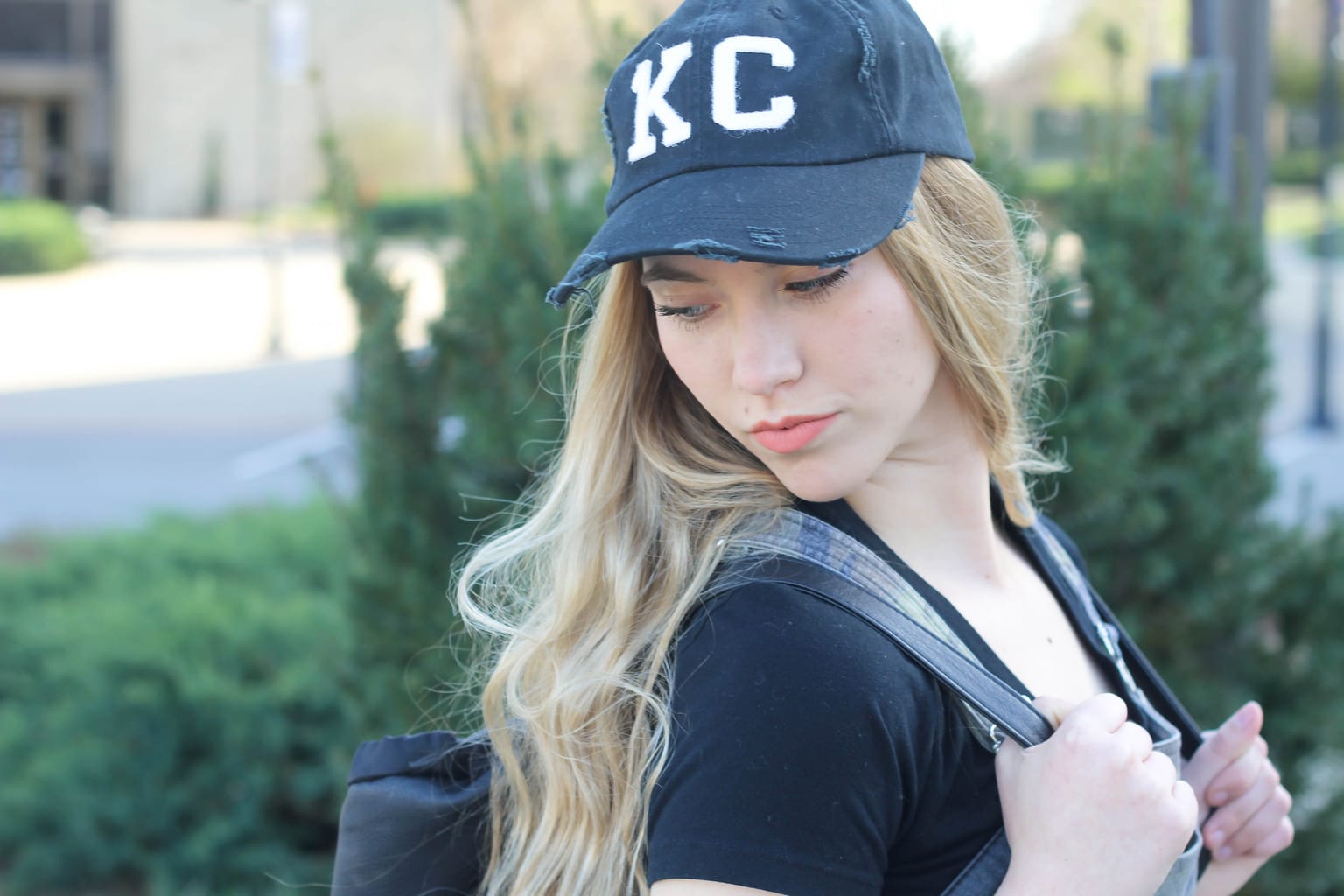 Monica's tattered and worn black ballcap has "KC" patches on the front.